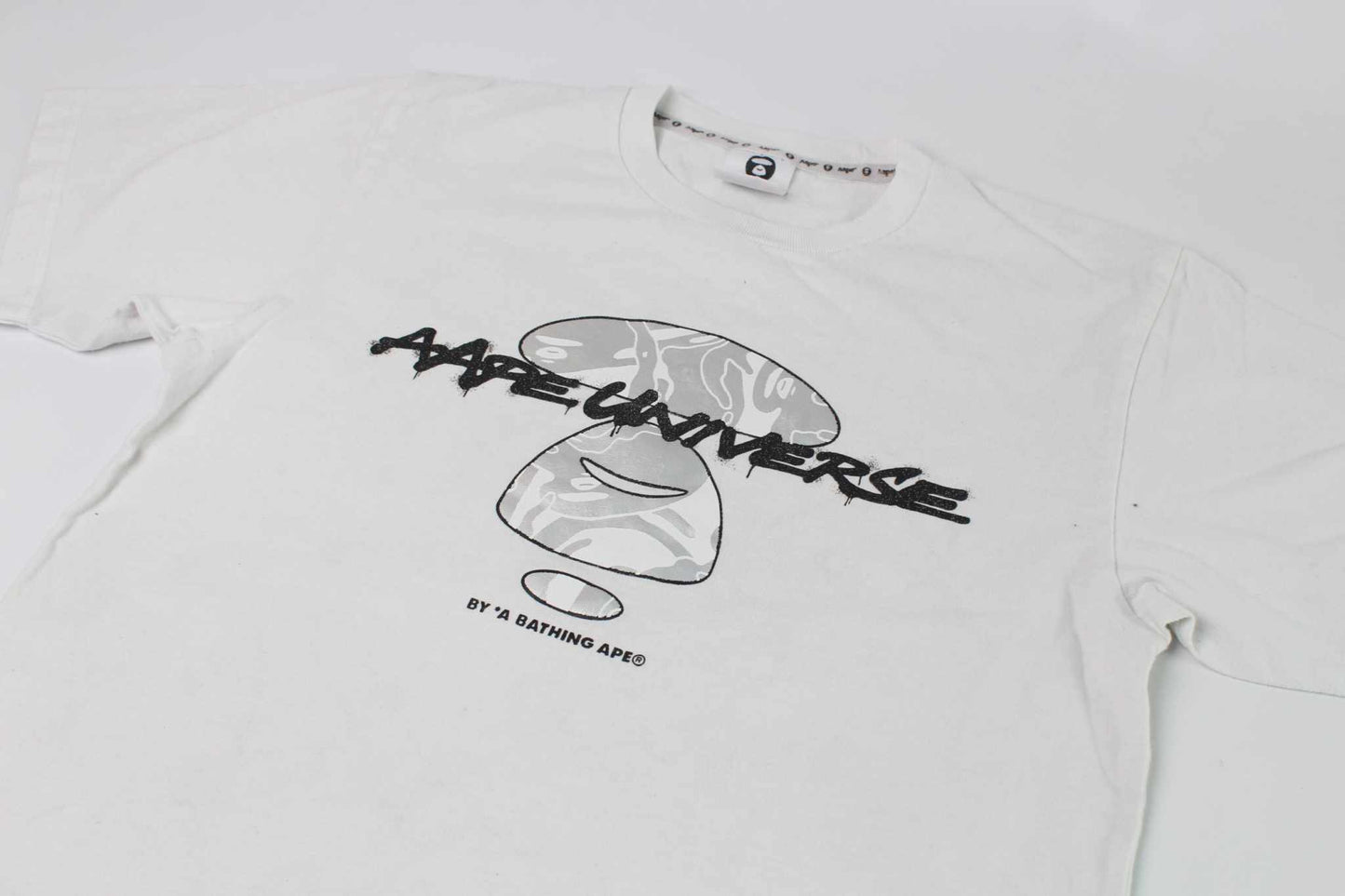 BAPE AAPE Laser Foil Camo Stencil Face Tee in white and silver, 100% cotton, size S-M, condition 9/10.