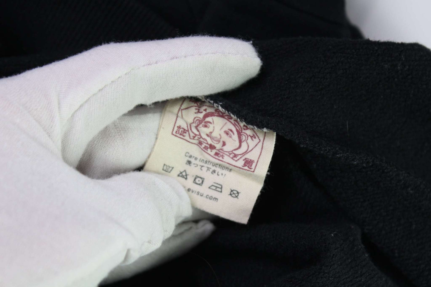 Close-up of the label on an EVISU black crewneck sweater.